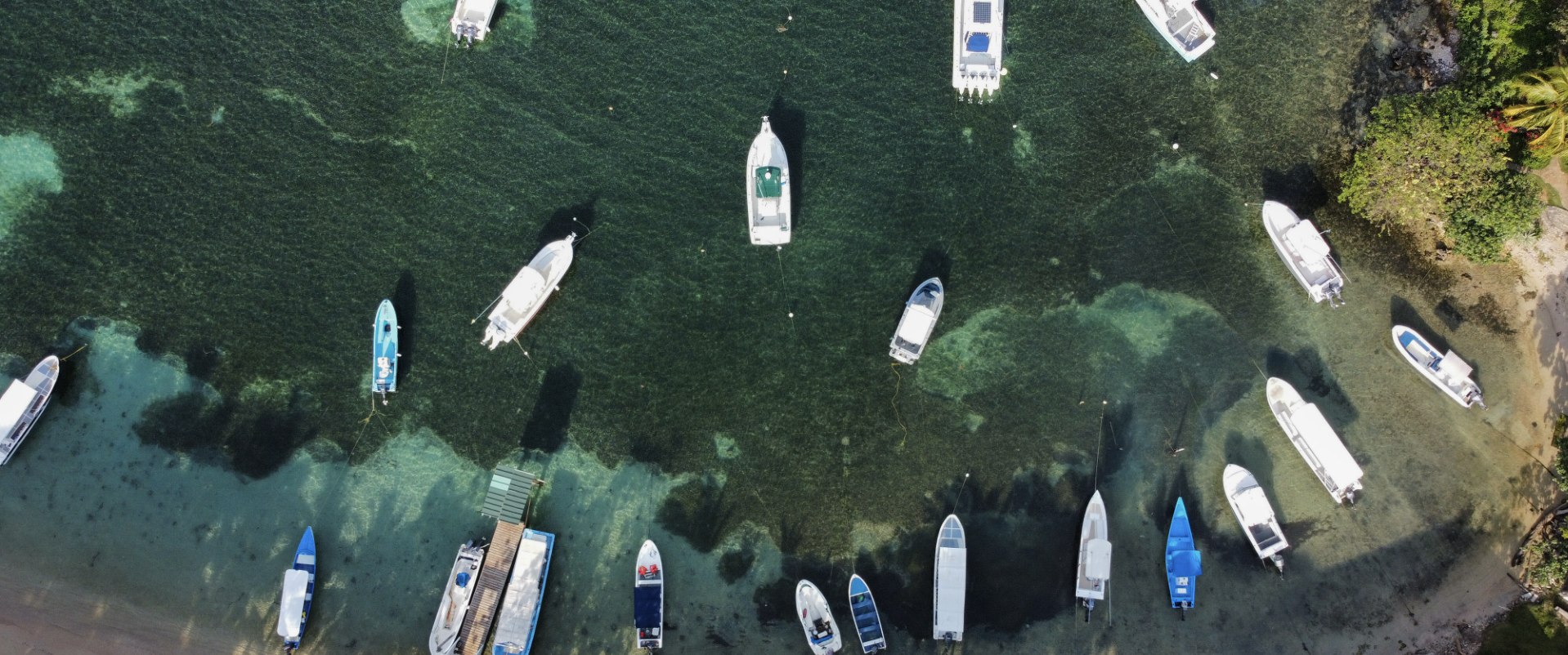 Boats moored over the reef, seen from above, the beach and palms below